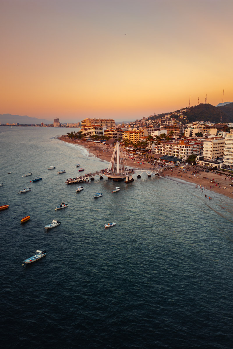 Los Muertos Beach Pier with boats sitting in bay looking up towards the romantic zone of Puerto Vallarta Mexico.